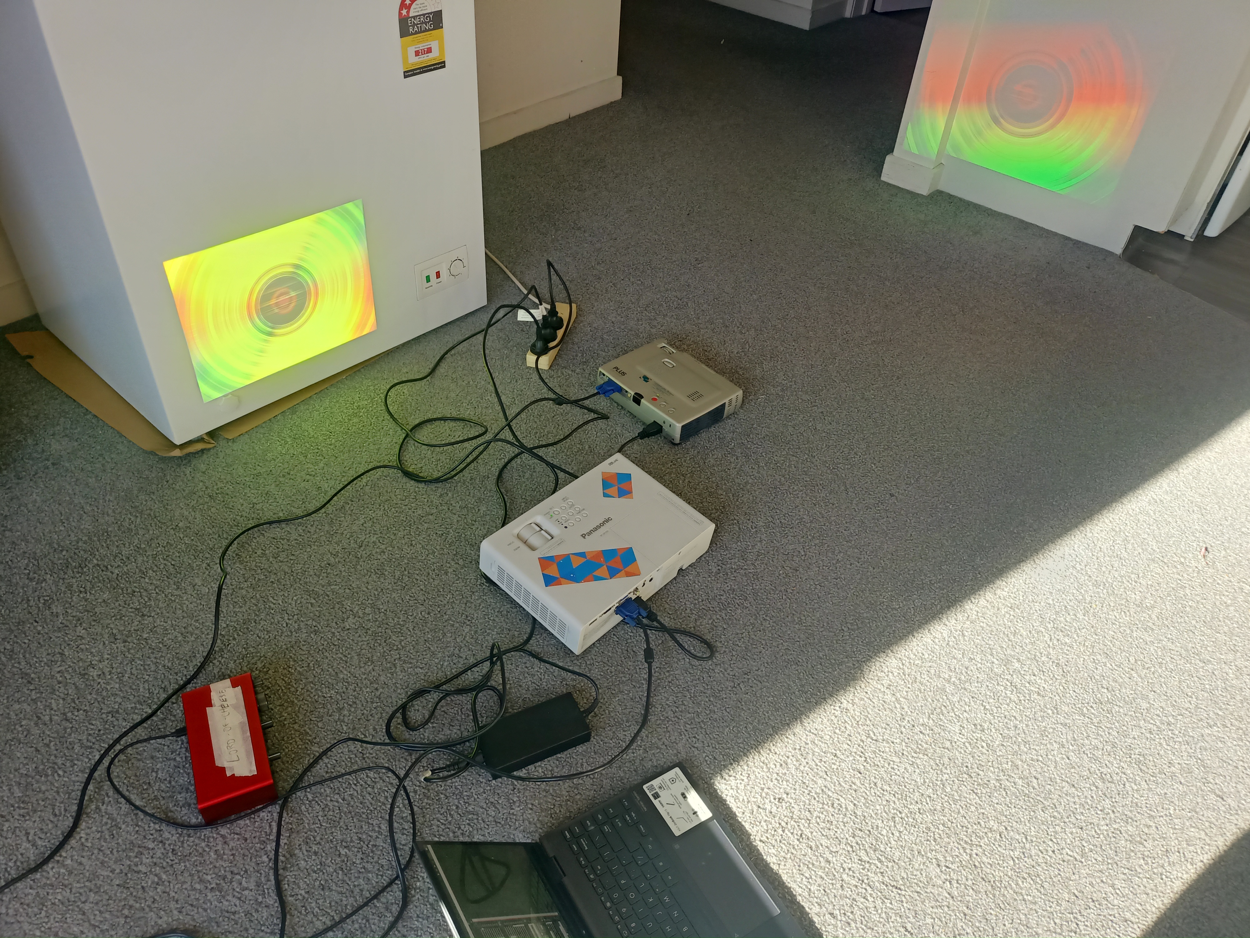 Projectors on the floor of a living room with sprawled cables on the ground connecting to various bits and bobs.